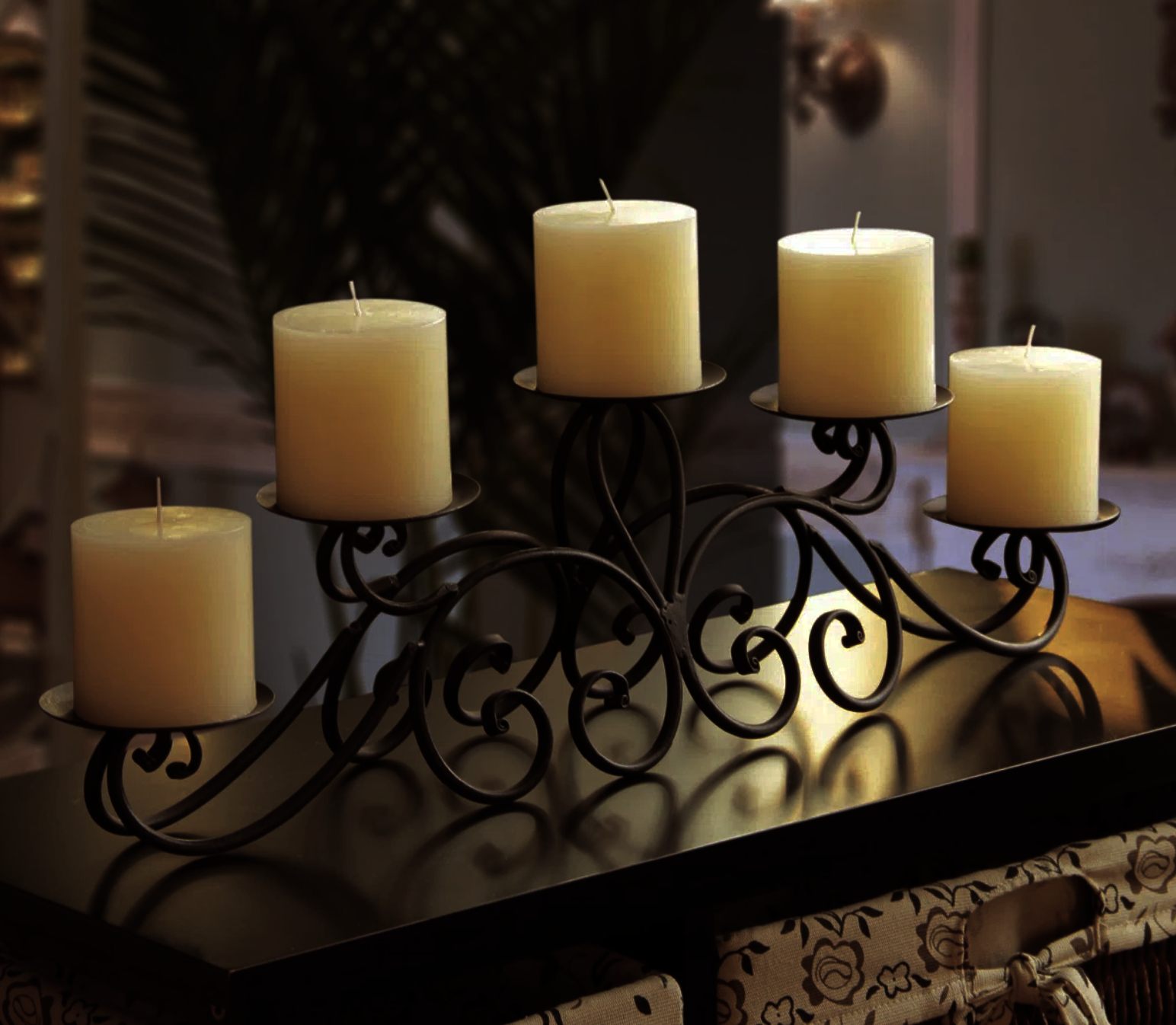 Black wrought iron candle holder with five ivory pillar candles on a dark surface, set in a warm, softly lit room